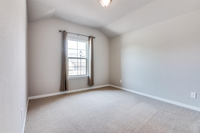 carpeted spare room featuring vaulted ceiling and baseboards