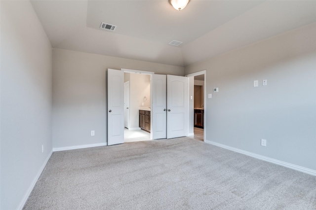 unfurnished bedroom with lofted ceiling, visible vents, baseboards, and light colored carpet