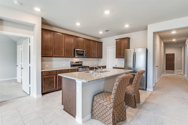 kitchen with stainless steel appliances, visible vents, a kitchen island with sink, a sink, and light carpet