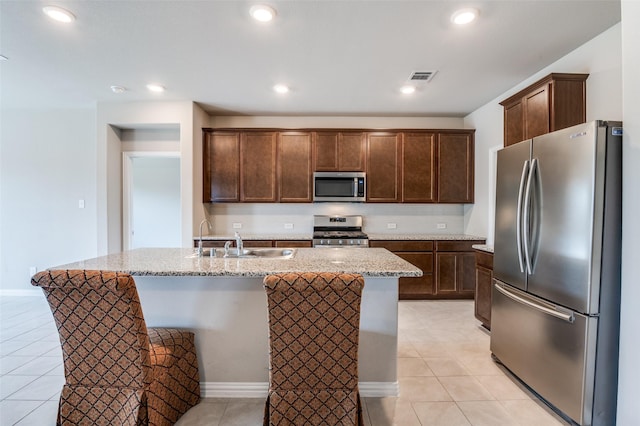 kitchen with an island with sink, light stone counters, stainless steel appliances, a sink, and light tile patterned flooring