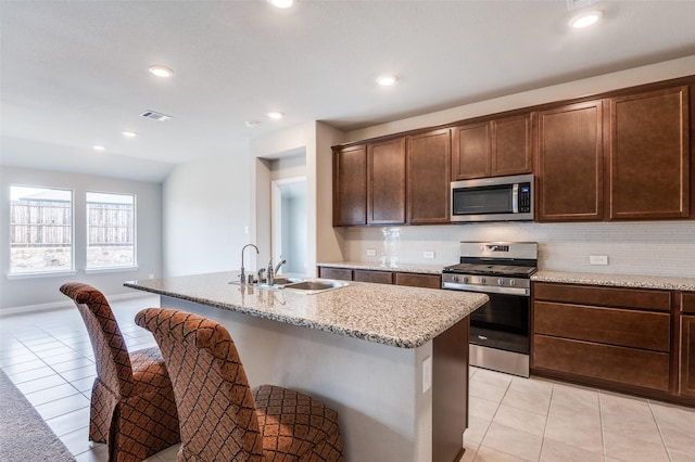 kitchen featuring light stone counters, a center island with sink, visible vents, decorative backsplash, and appliances with stainless steel finishes