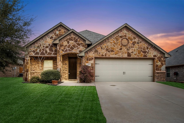 french provincial home with a lawn, stone siding, concrete driveway, a garage, and brick siding