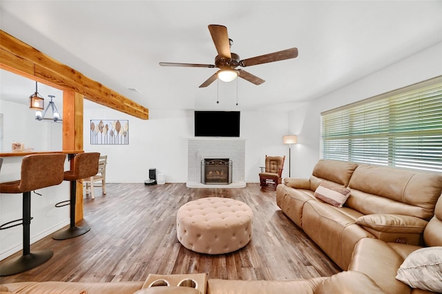 living room with beam ceiling, a ceiling fan, a brick fireplace, wood finished floors, and baseboards