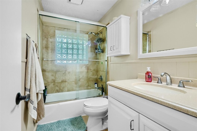 bathroom featuring toilet, shower / bath combination with glass door, wainscoting, and vanity