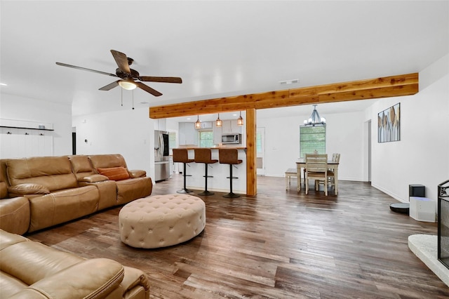 living room with ceiling fan with notable chandelier, dark wood-style flooring, visible vents, baseboards, and beamed ceiling