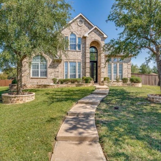 traditional home featuring brick siding, fence, and a front lawn