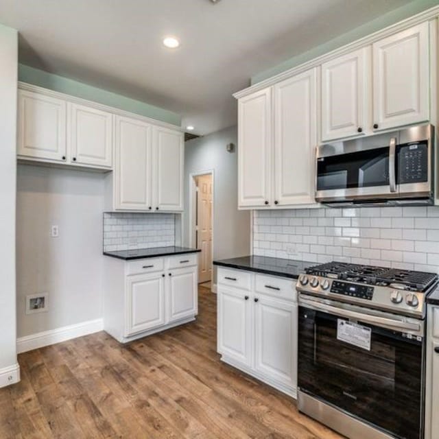 kitchen with baseboards, dark countertops, appliances with stainless steel finishes, light wood-type flooring, and white cabinetry