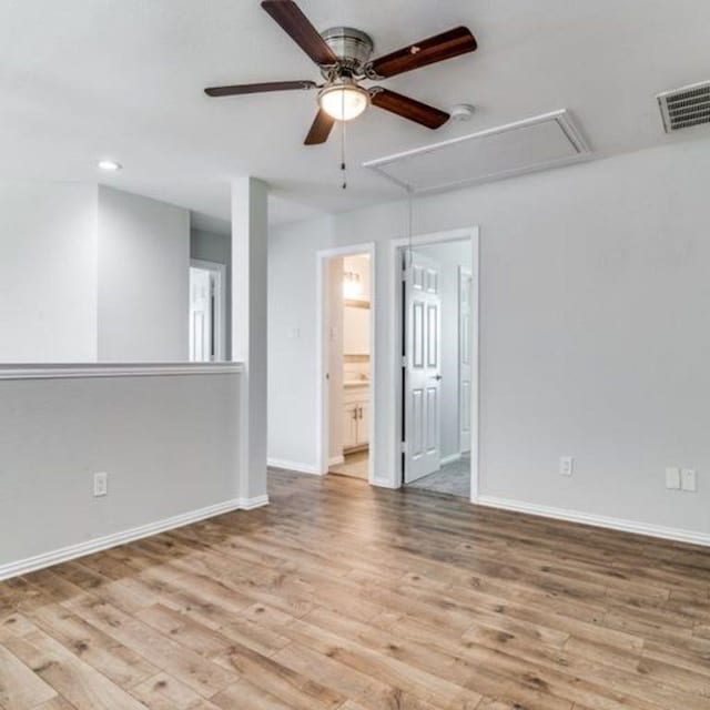 unfurnished room featuring light wood finished floors, attic access, visible vents, baseboards, and a ceiling fan