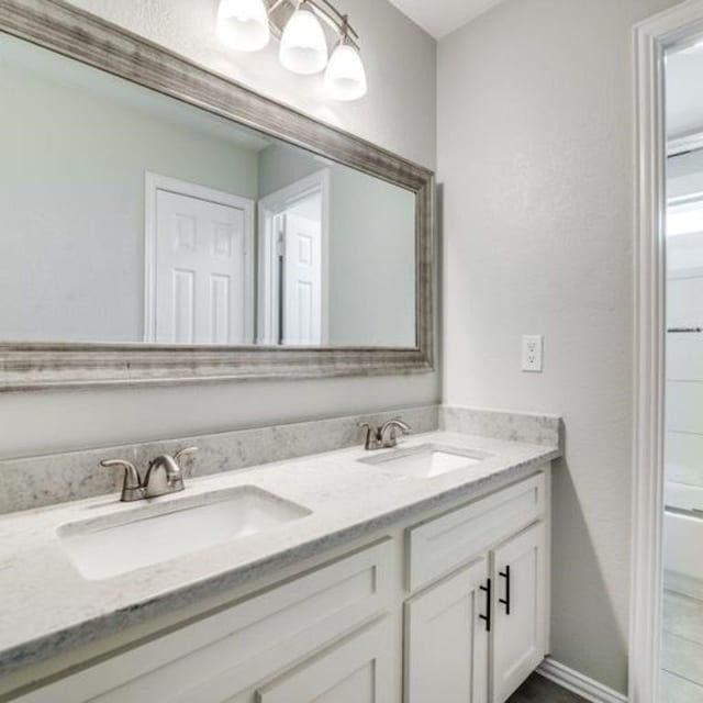 bathroom featuring  shower combination, double vanity, a sink, and baseboards