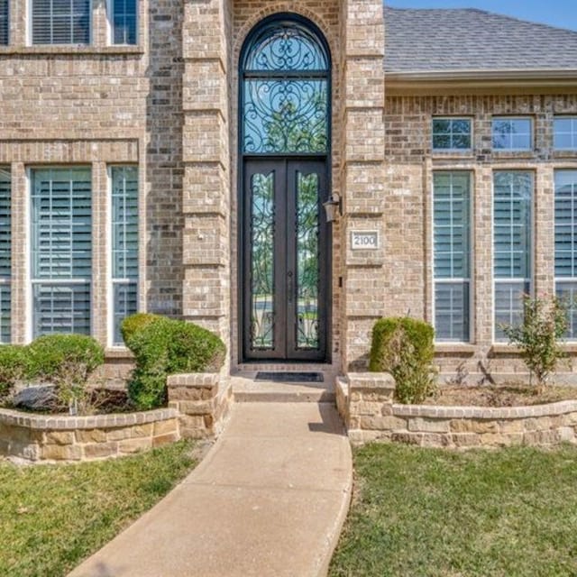 view of exterior entry featuring brick siding, roof with shingles, and french doors