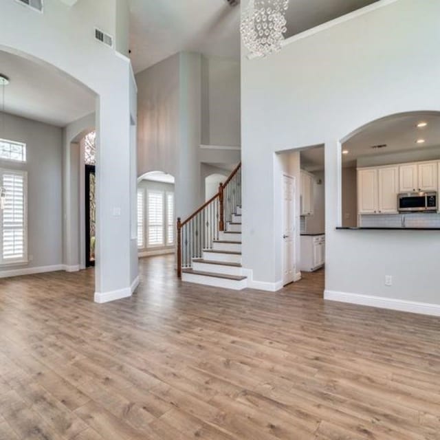 unfurnished living room with light wood finished floors, stairway, baseboards, and arched walkways