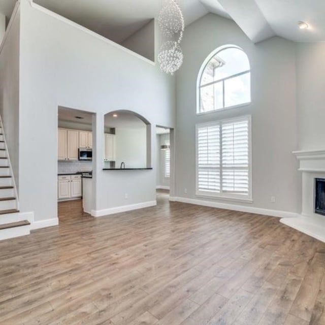 unfurnished living room with stairway, light wood-style flooring, a glass covered fireplace, a chandelier, and baseboards