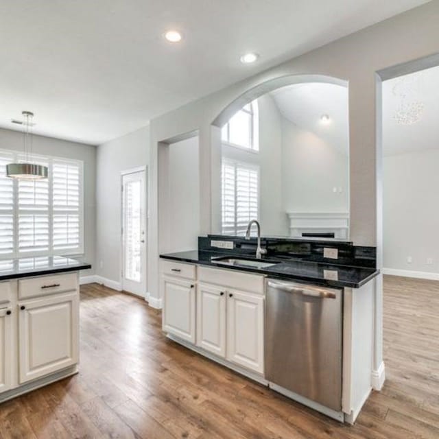 kitchen featuring stainless steel dishwasher, dark countertops, a sink, and white cabinets