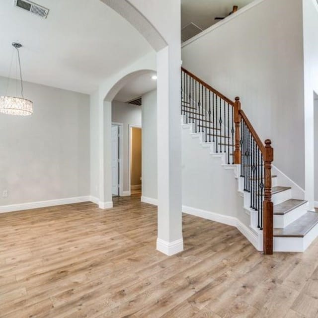 interior space featuring light wood-type flooring, arched walkways, visible vents, and baseboards