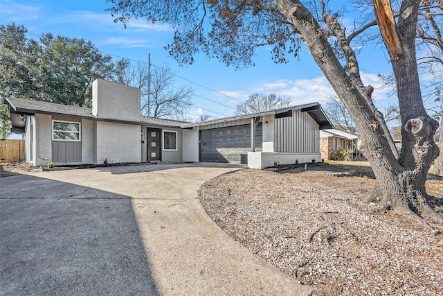 mid-century modern home with concrete driveway, a chimney, an attached garage, board and batten siding, and brick siding