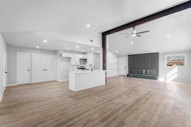 unfurnished living room with lofted ceiling with beams, light wood-type flooring, visible vents, and baseboards