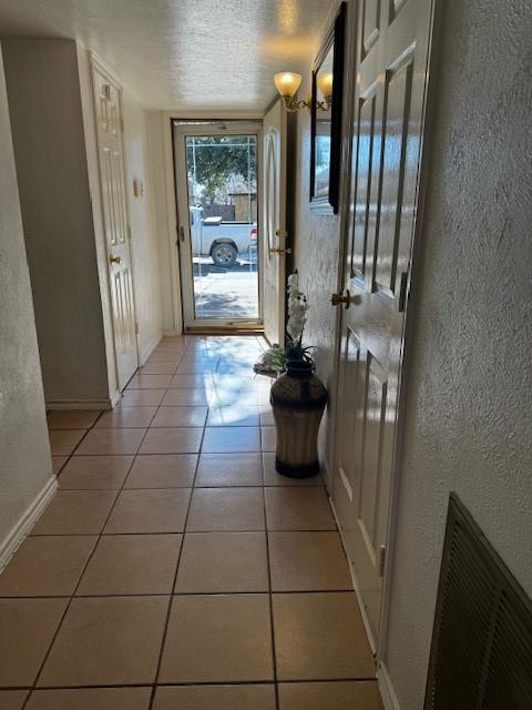 doorway to outside with visible vents, a textured wall, and light tile patterned floors