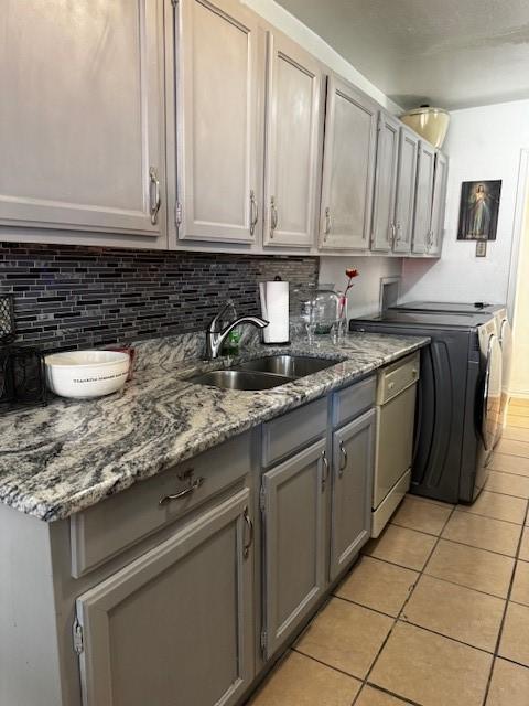 kitchen featuring light tile patterned floors, white dishwasher, a sink, gray cabinets, and backsplash