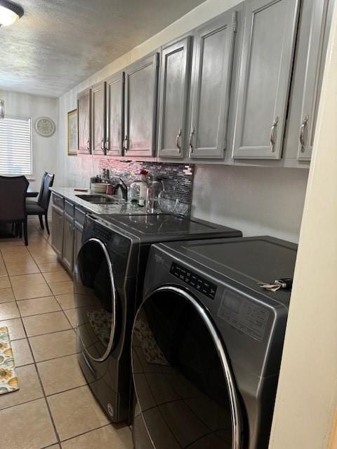 clothes washing area with a textured ceiling, light tile patterned flooring, a sink, cabinet space, and washing machine and clothes dryer