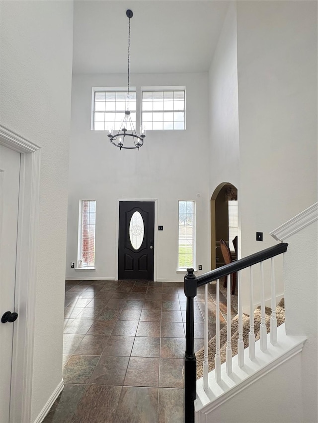 foyer featuring arched walkways, a notable chandelier, a high ceiling, and baseboards