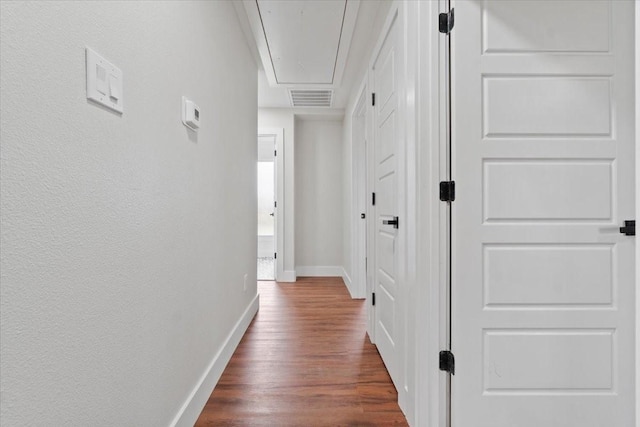 hallway with baseboards, attic access, visible vents, and dark wood-style flooring