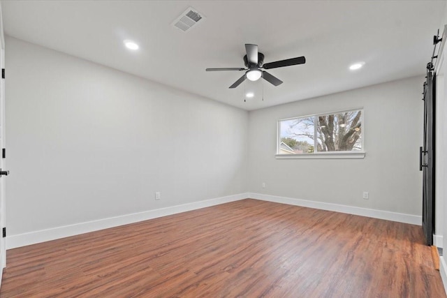 spare room with a barn door, baseboards, a ceiling fan, and wood finished floors