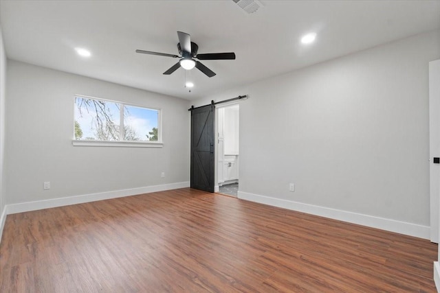 unfurnished bedroom featuring a barn door, wood finished floors, visible vents, and baseboards