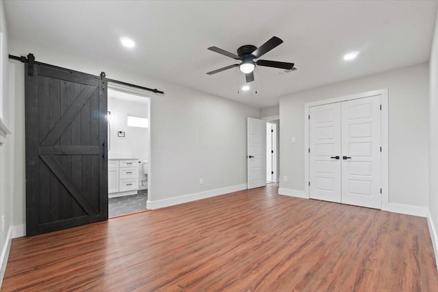 unfurnished bedroom featuring a barn door, dark wood-style flooring, and baseboards