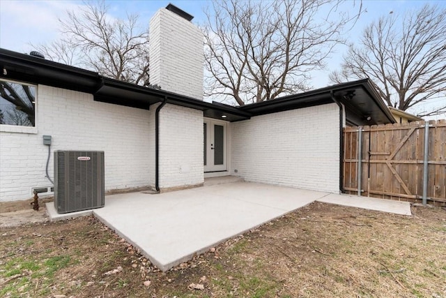 view of side of home featuring a patio, brick siding, a chimney, and central air condition unit