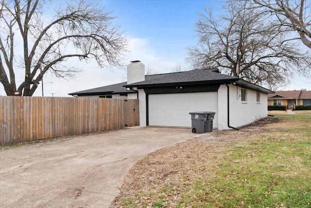 view of side of home with concrete driveway, brick siding, fence, and a chimney