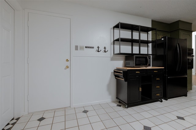 kitchen featuring black appliances, a textured ceiling, dark cabinets, and a wainscoted wall