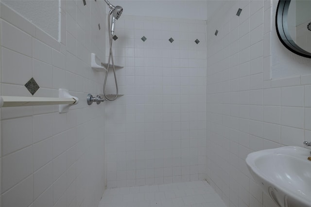 full bath featuring tiled shower, a sink, and tile walls