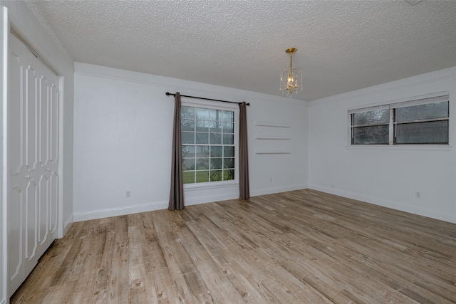 unfurnished room featuring light wood-type flooring, an inviting chandelier, baseboards, and a textured ceiling