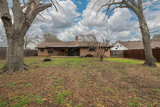 back of house featuring a chimney, brick siding, a yard, and a fenced backyard