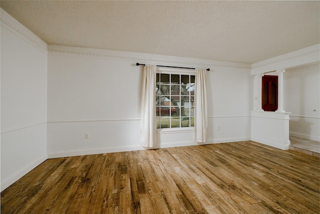 empty room with crown molding, a textured ceiling, baseboards, and wood finished floors