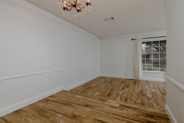 unfurnished room featuring a chandelier, a textured ceiling, wood finished floors, visible vents, and ornamental molding