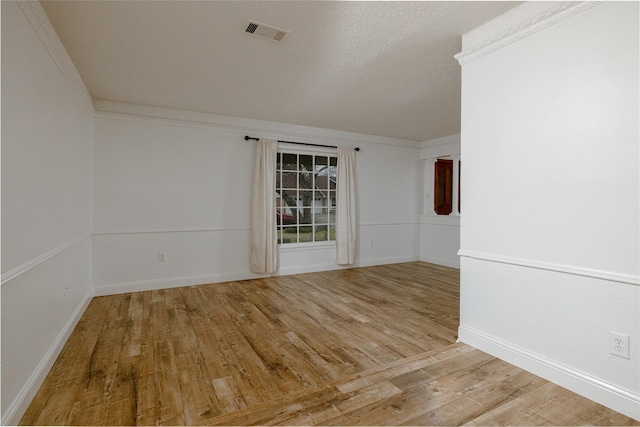 unfurnished room featuring a textured ceiling, light wood-style flooring, visible vents, baseboards, and ornamental molding