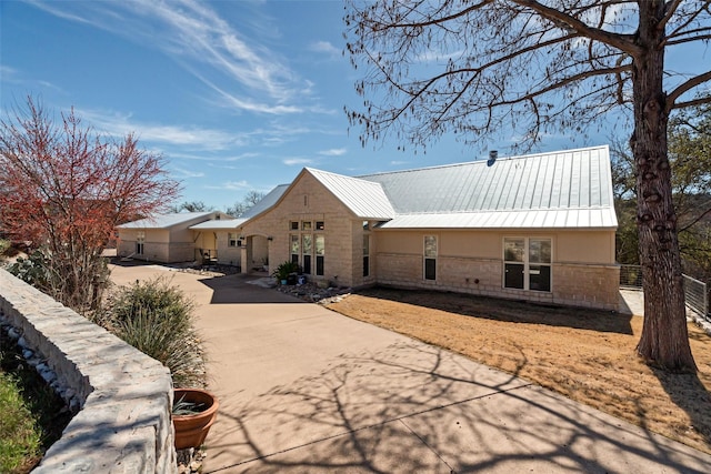 exterior space featuring metal roof, stone siding, concrete driveway, and stucco siding