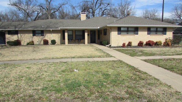 ranch-style home featuring brick siding, a chimney, a front lawn, and roof with shingles