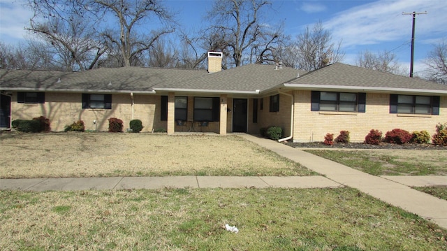 ranch-style home featuring brick siding, a chimney, a front yard, and a shingled roof