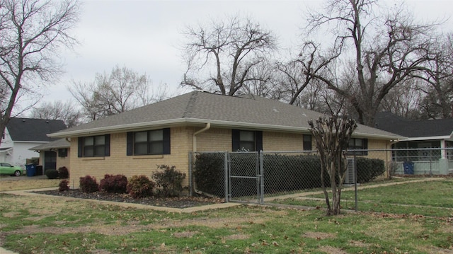 view of property exterior featuring a shingled roof, brick siding, a lawn, and fence