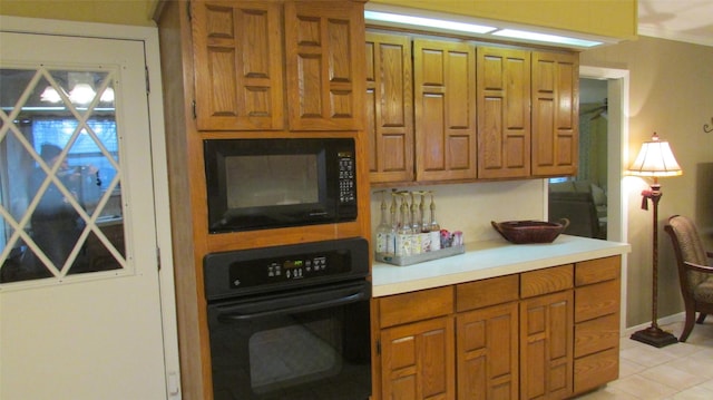 kitchen with brown cabinetry, light countertops, black appliances, and light tile patterned flooring