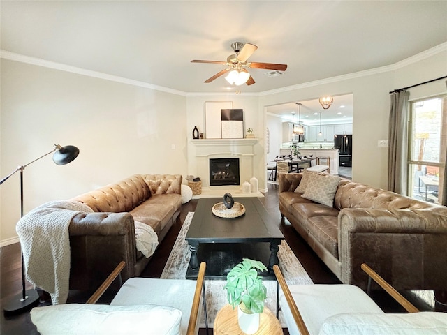 living room featuring a fireplace with raised hearth, wood finished floors, a ceiling fan, and crown molding