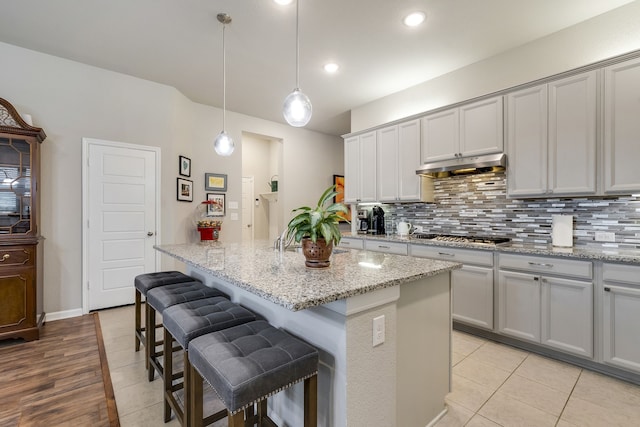 kitchen featuring pendant lighting, gray cabinets, stainless steel gas stovetop, a kitchen island, and under cabinet range hood