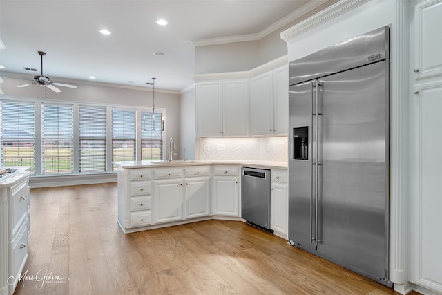 kitchen with decorative light fixtures, stainless steel appliances, light countertops, white cabinets, and a sink