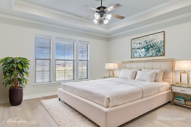 bedroom featuring baseboards, a ceiling fan, ornamental molding, a tray ceiling, and light wood-type flooring