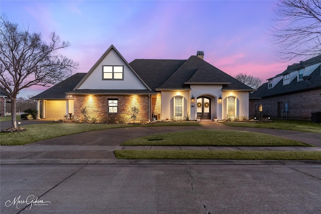 view of front of property with a front yard, stucco siding, a chimney, curved driveway, and a garage