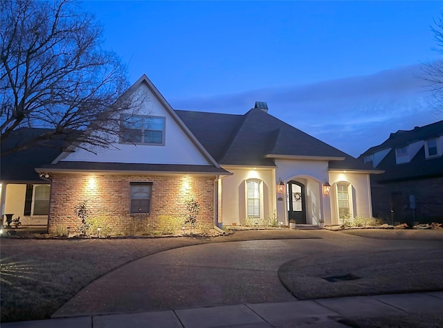 view of front facade with driveway, brick siding, and stucco siding