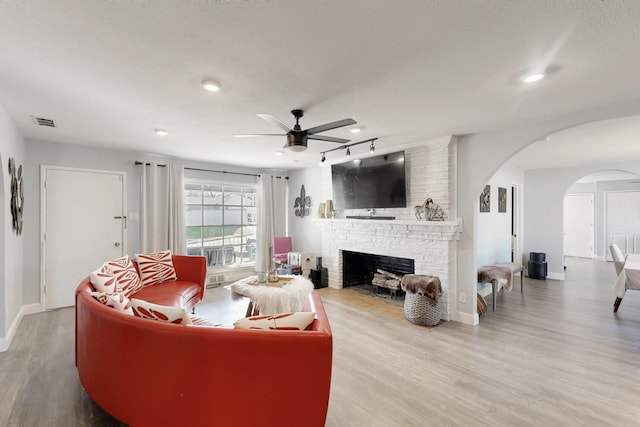 living room featuring a fireplace, visible vents, arched walkways, and wood finished floors