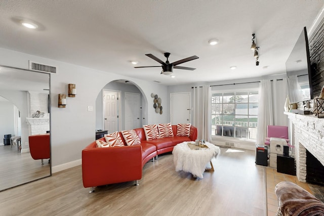 living area featuring arched walkways, a large fireplace, visible vents, baseboards, and light wood finished floors